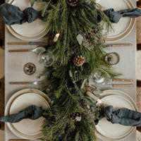 Blue Christmas garland with blue spruce, seeded eucalyptus and pinecones down a linen table with dark napkins