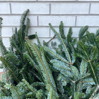 Stack of green fresh Christmas tree branches on a white metal grid background